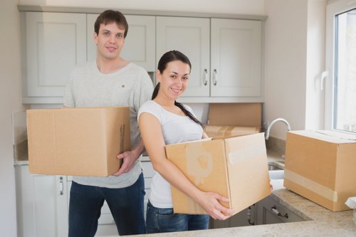 Professional movers carrying household items through a narrow entry in Queens Park